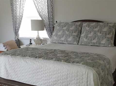 Bedroom featuring a bed next to a window with blinds and drapes.